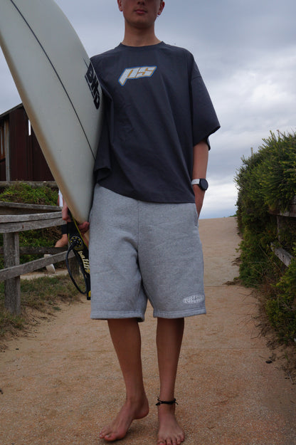 Person holding a surfboard with a cloudy sky and outdoor setting with pure surf offshore tshirt and pure surf fleece shorts 